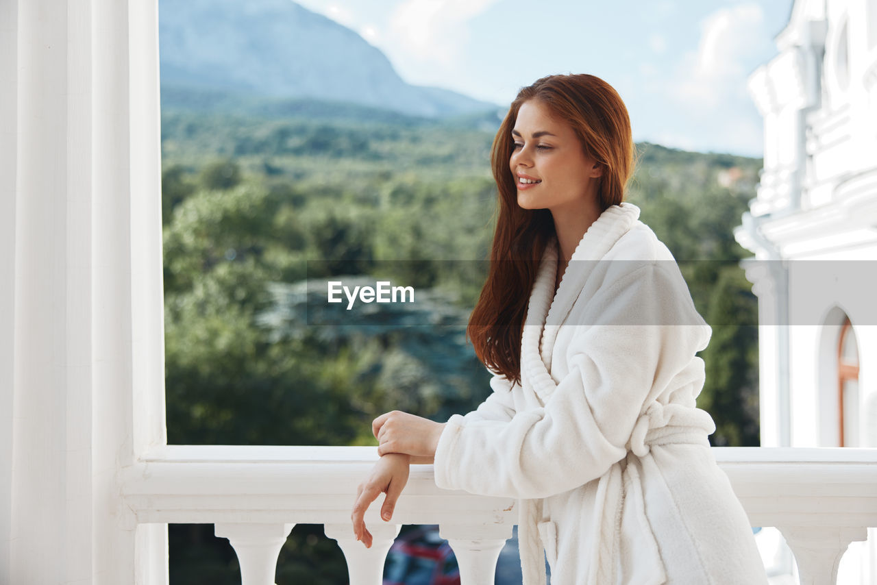 Portrait of young woman standing against window