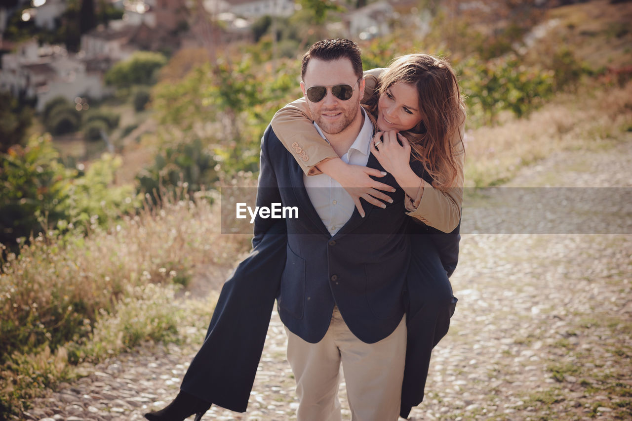 Portrait of man giving piggy back ride to happy woman standing on land