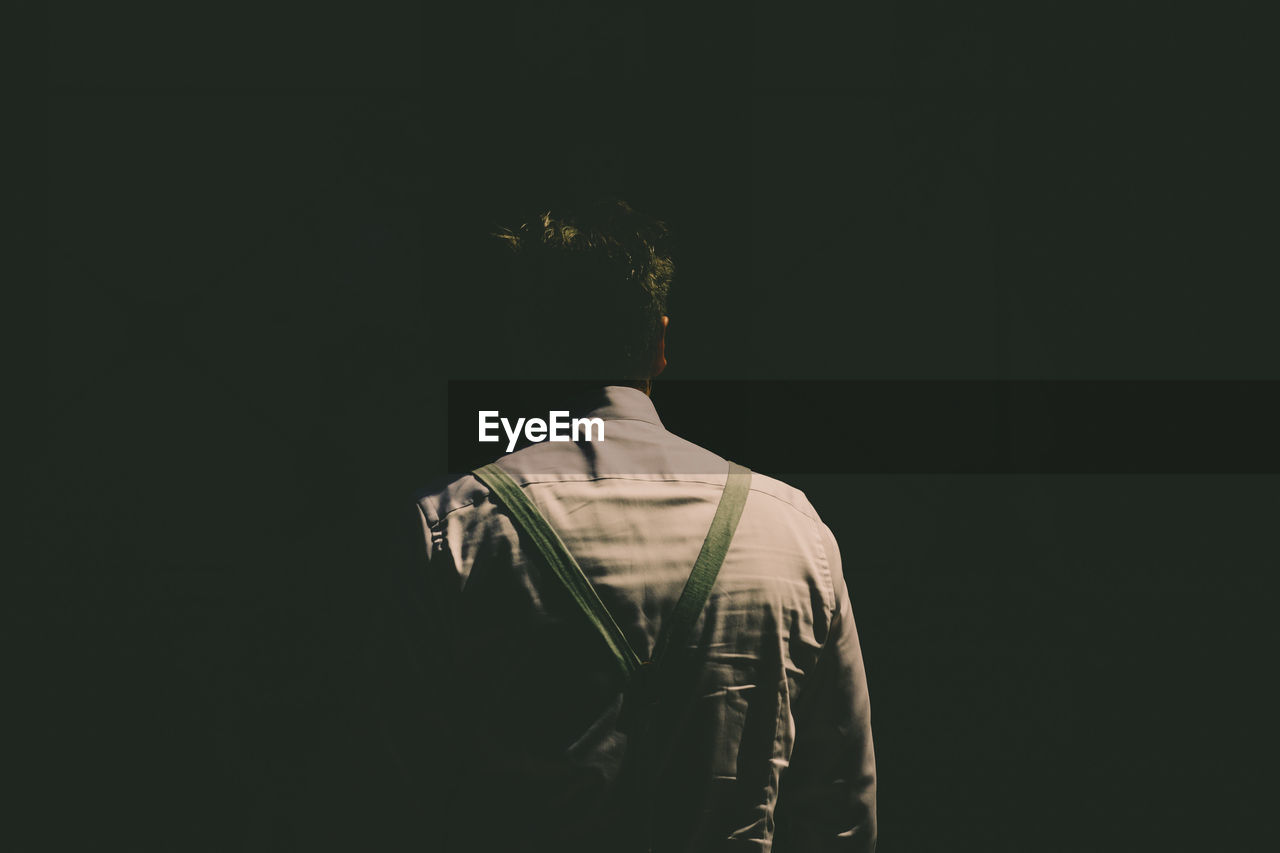 Rear view of man standing against black background