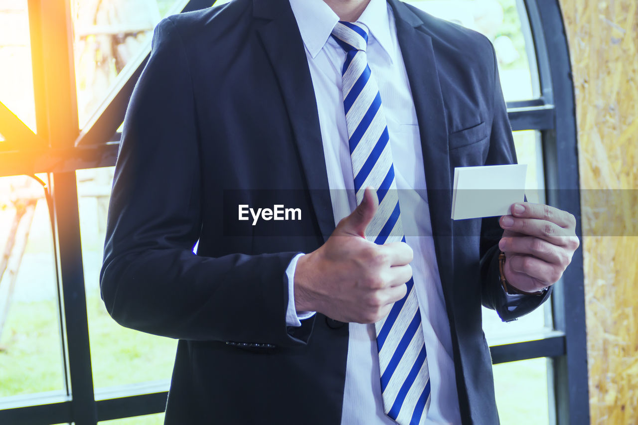 MIDSECTION OF MAN HOLDING CAMERA WHILE STANDING AT HOME