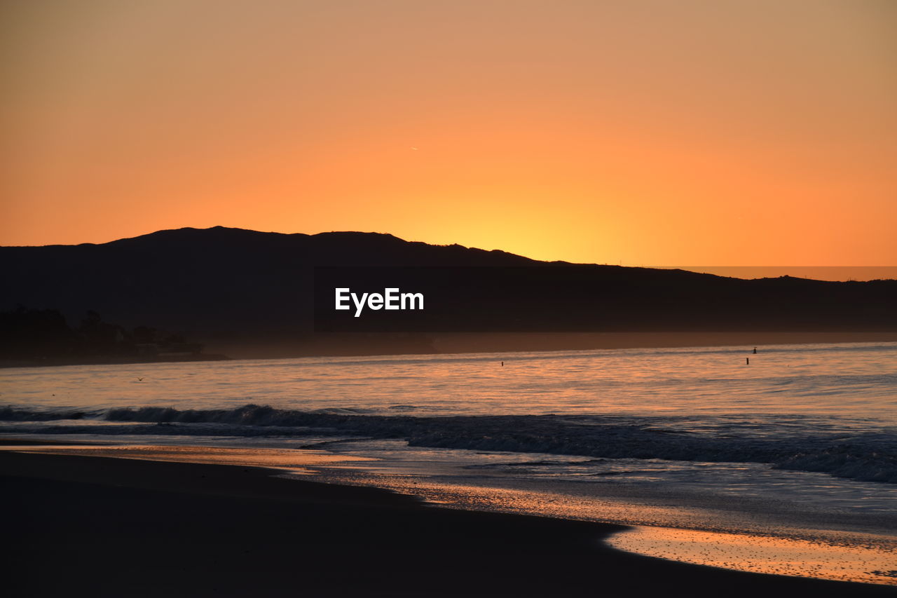 SCENIC VIEW OF SEA AGAINST SILHOUETTE MOUNTAINS DURING SUNSET