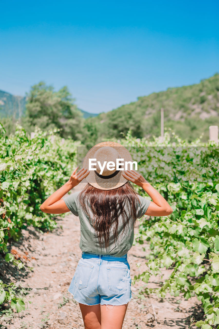 REAR VIEW OF WOMAN STANDING AGAINST PLANTS