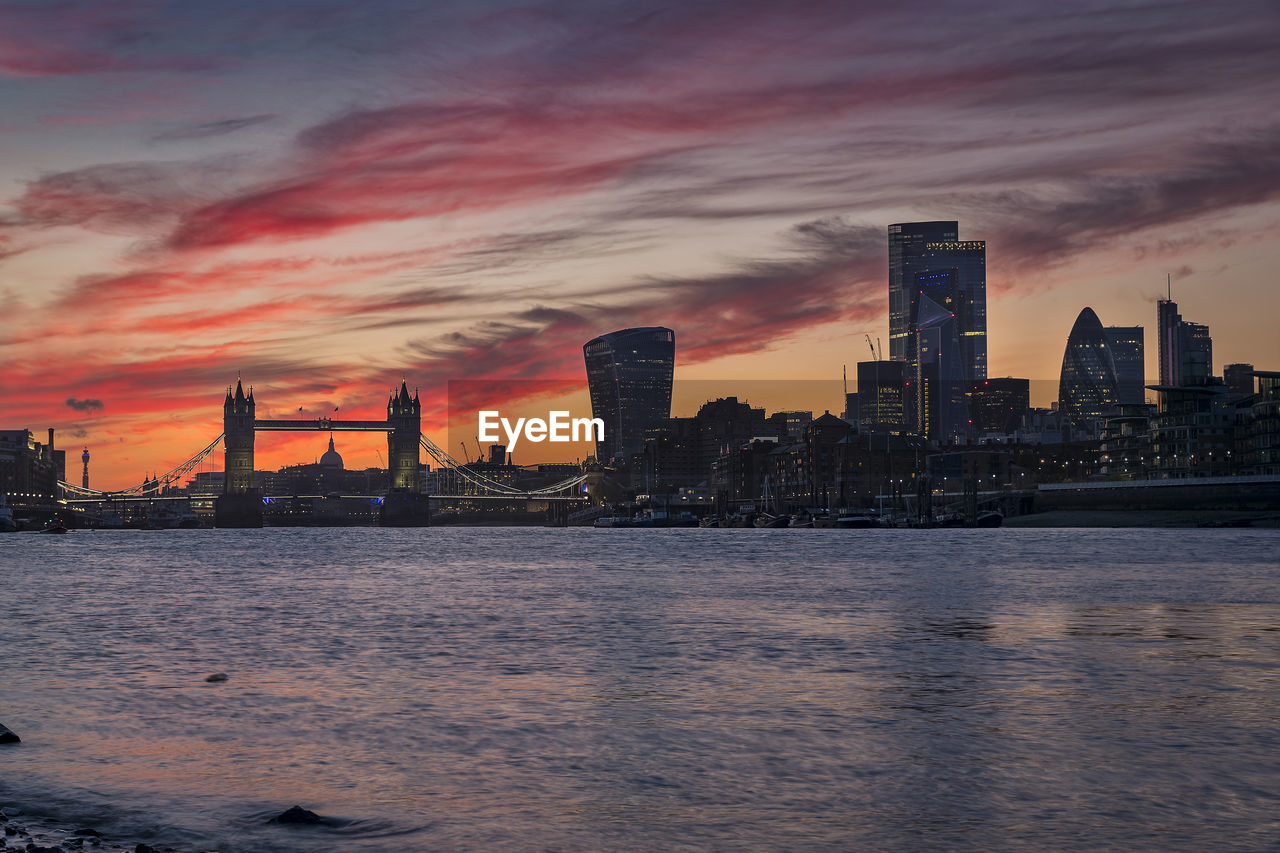 SEA BY CITY BUILDINGS AGAINST SKY DURING SUNSET