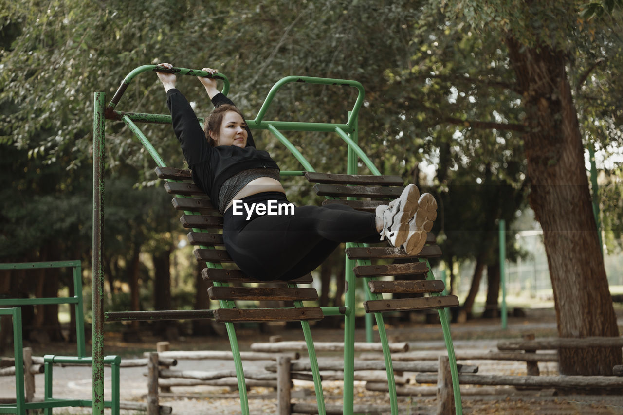 Smiling overweight young woman exercising at outdoor gym