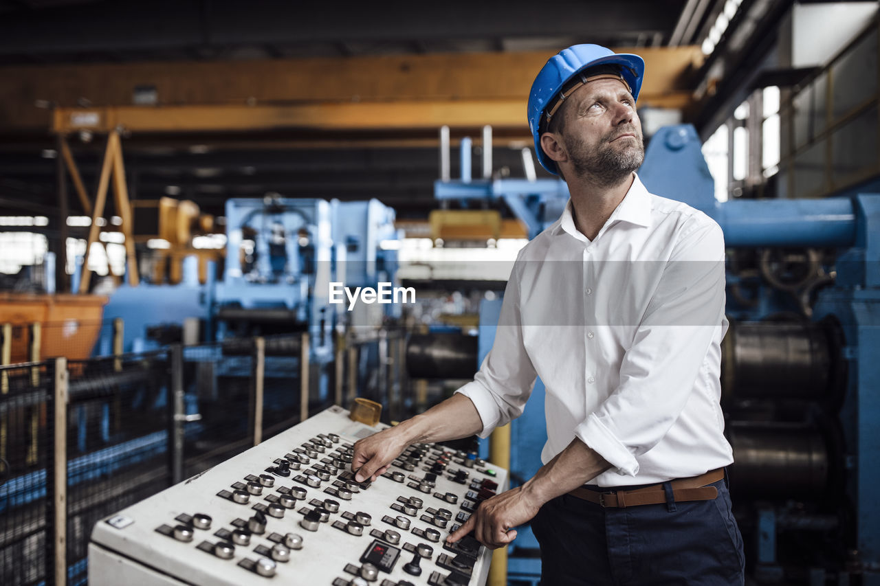 Male entrepreneur operating control panel looking up while standing at industry