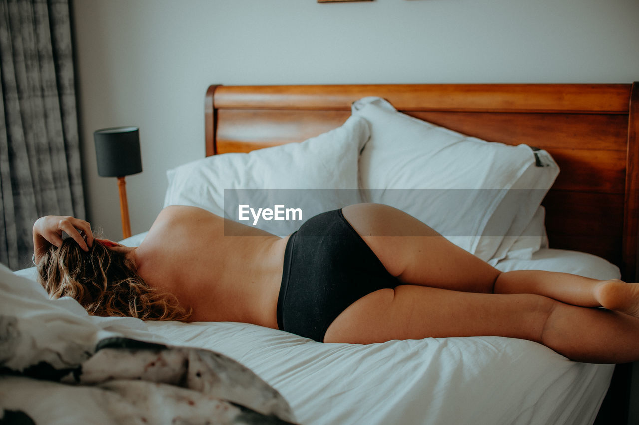 Rear view of shirtless woman lying on bed at home