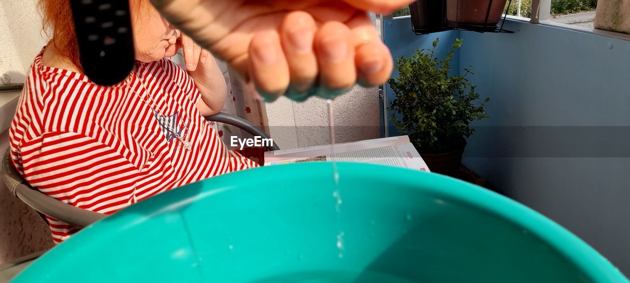 Close-up of water falling from hand in bucket with girl studying at background