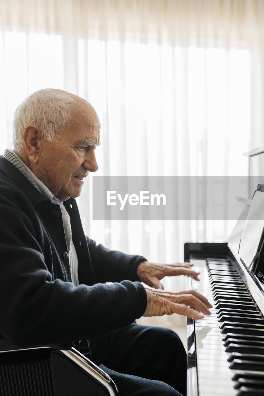 Senior man sitting in wheelchair playing piano at home