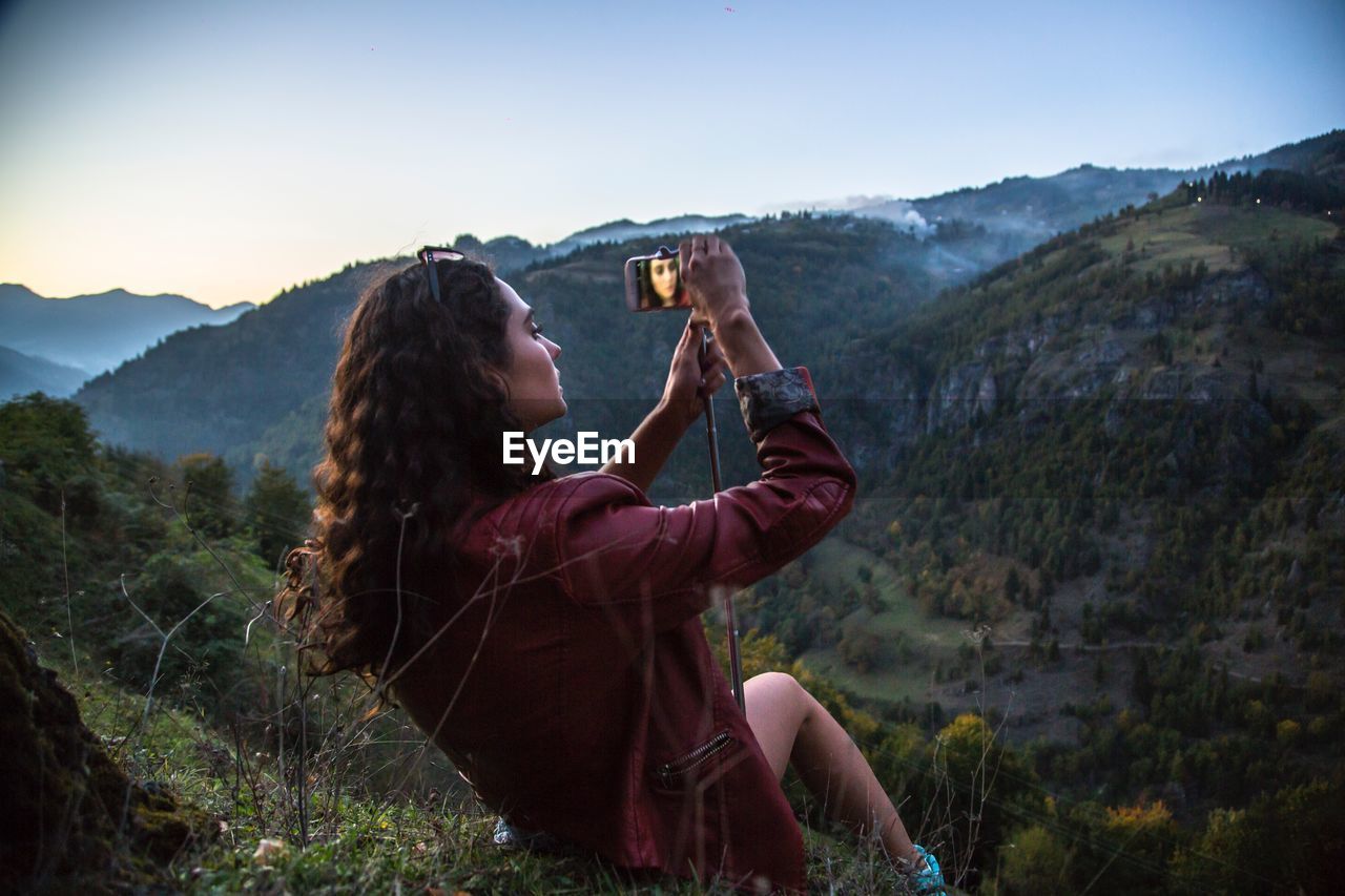 Young woman photographing while sitting on mountain