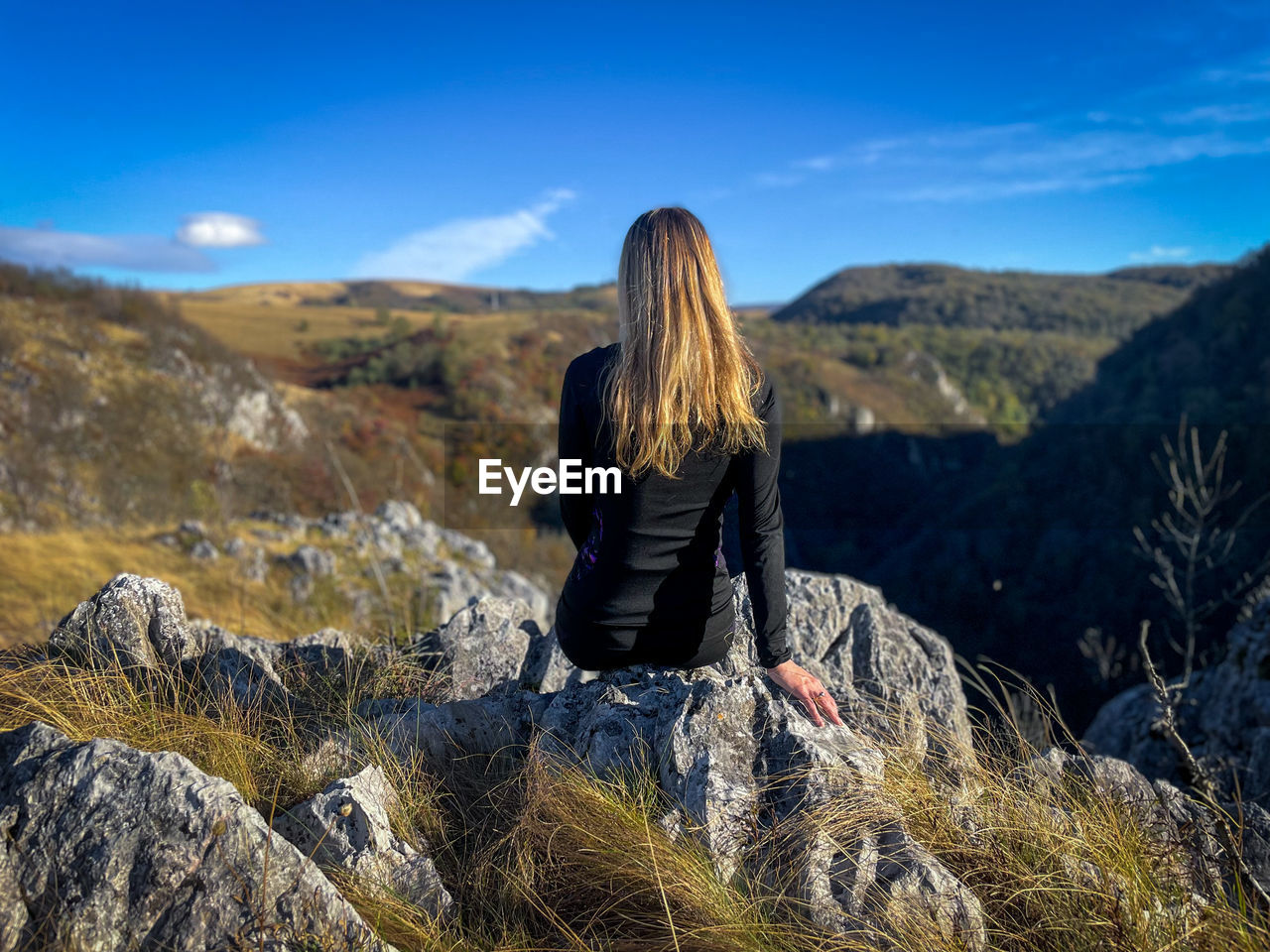 Rear view of fit woman resting on top of a cliff while looking at the mountains in the distance
