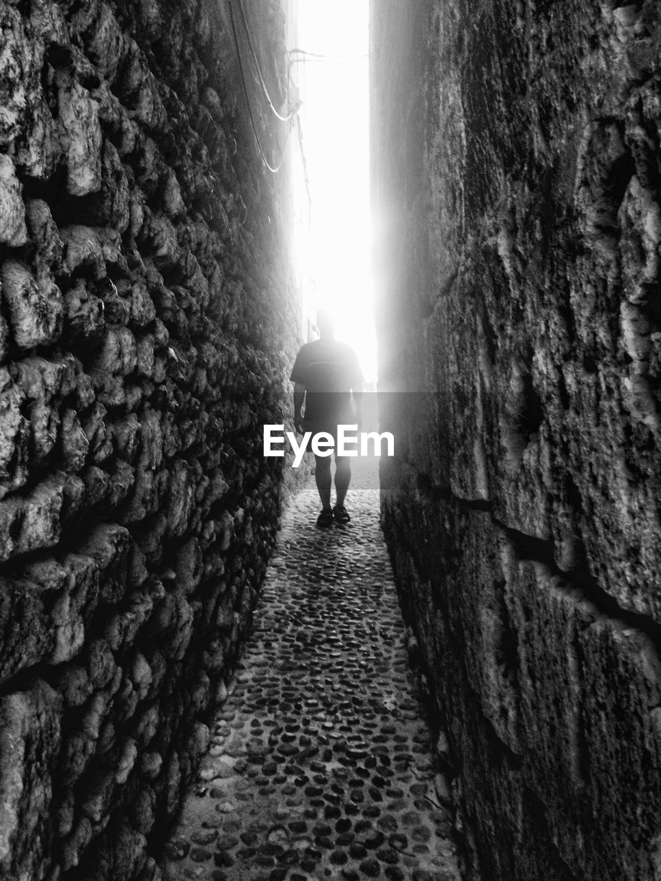 Man standing on alley amidst stone wall