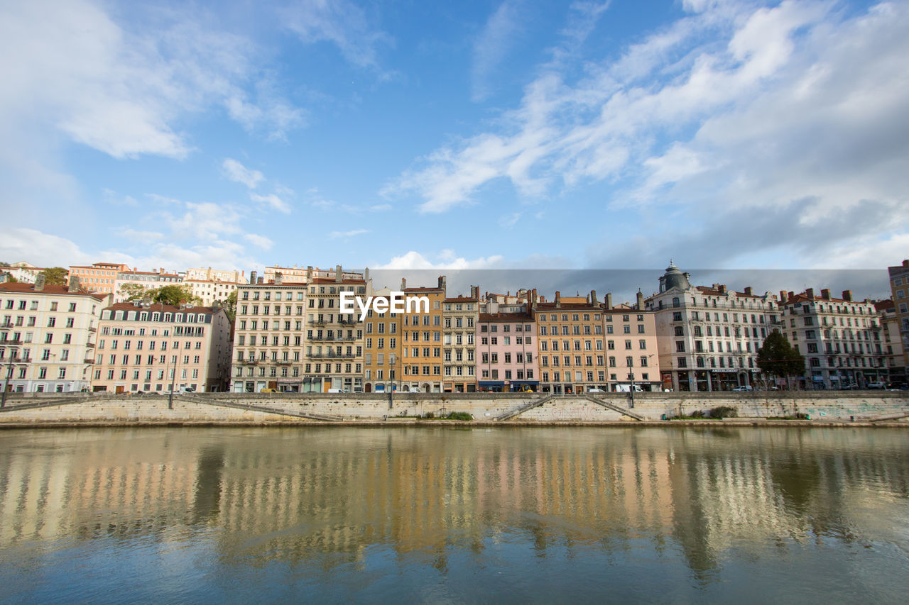 Buildings by river against sky in city