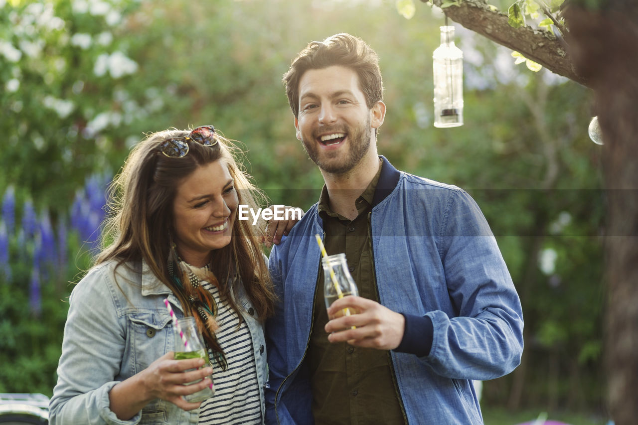 Portrait of happy man enjoying with woman while holding drink bottles at summer party