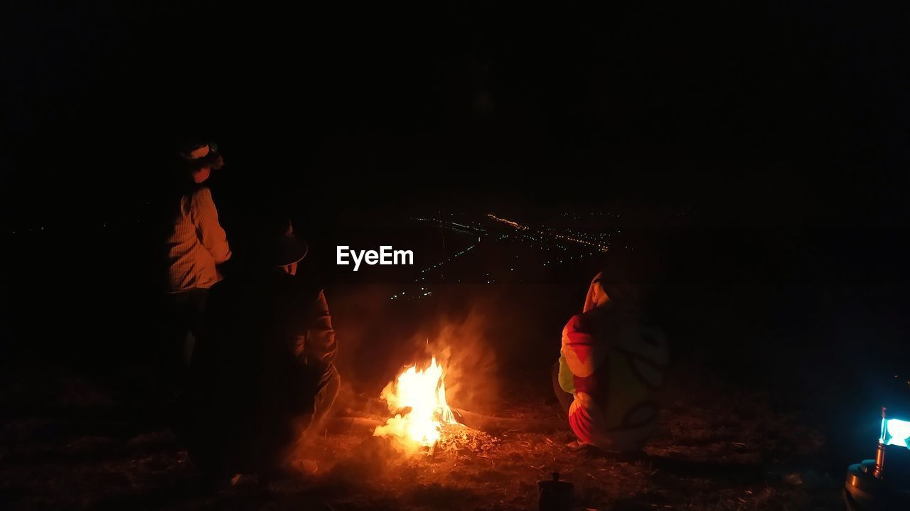 Rear view of people sitting by bonfire at night