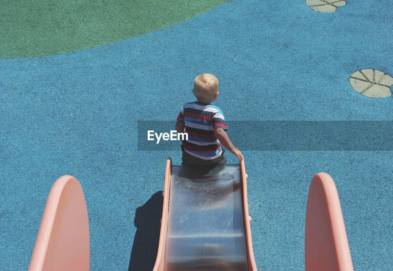 Rear view of boy playing on slide at playground