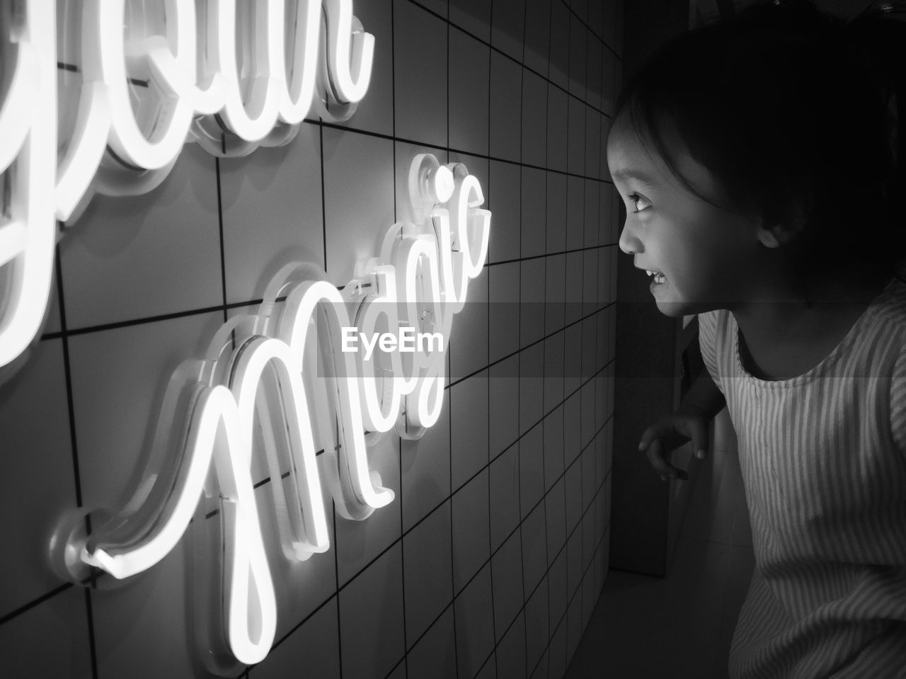 Smiling girl looking at illuminated text on wall