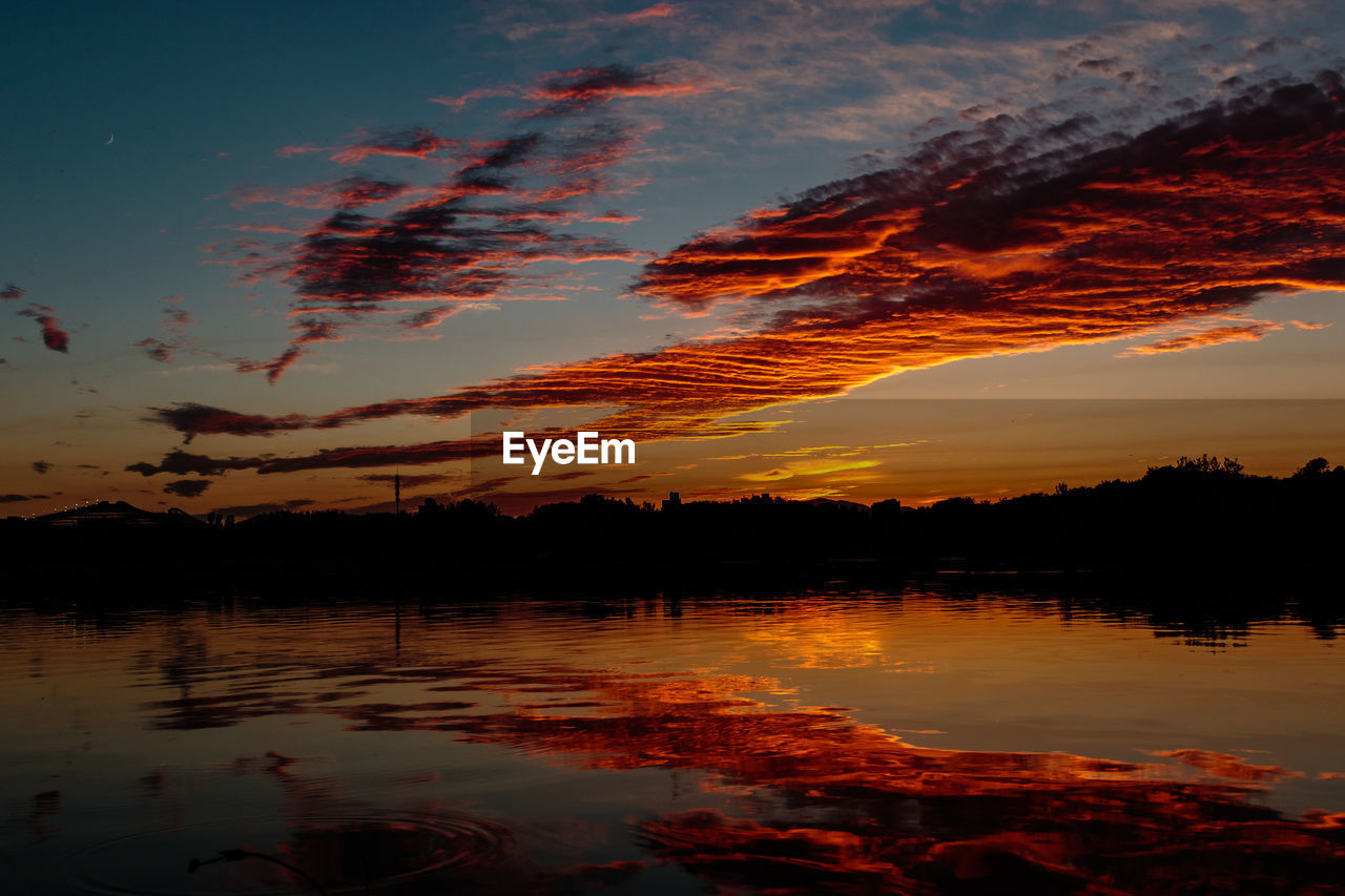 SCENIC VIEW OF LAKE AGAINST CLOUDY SKY DURING SUNSET