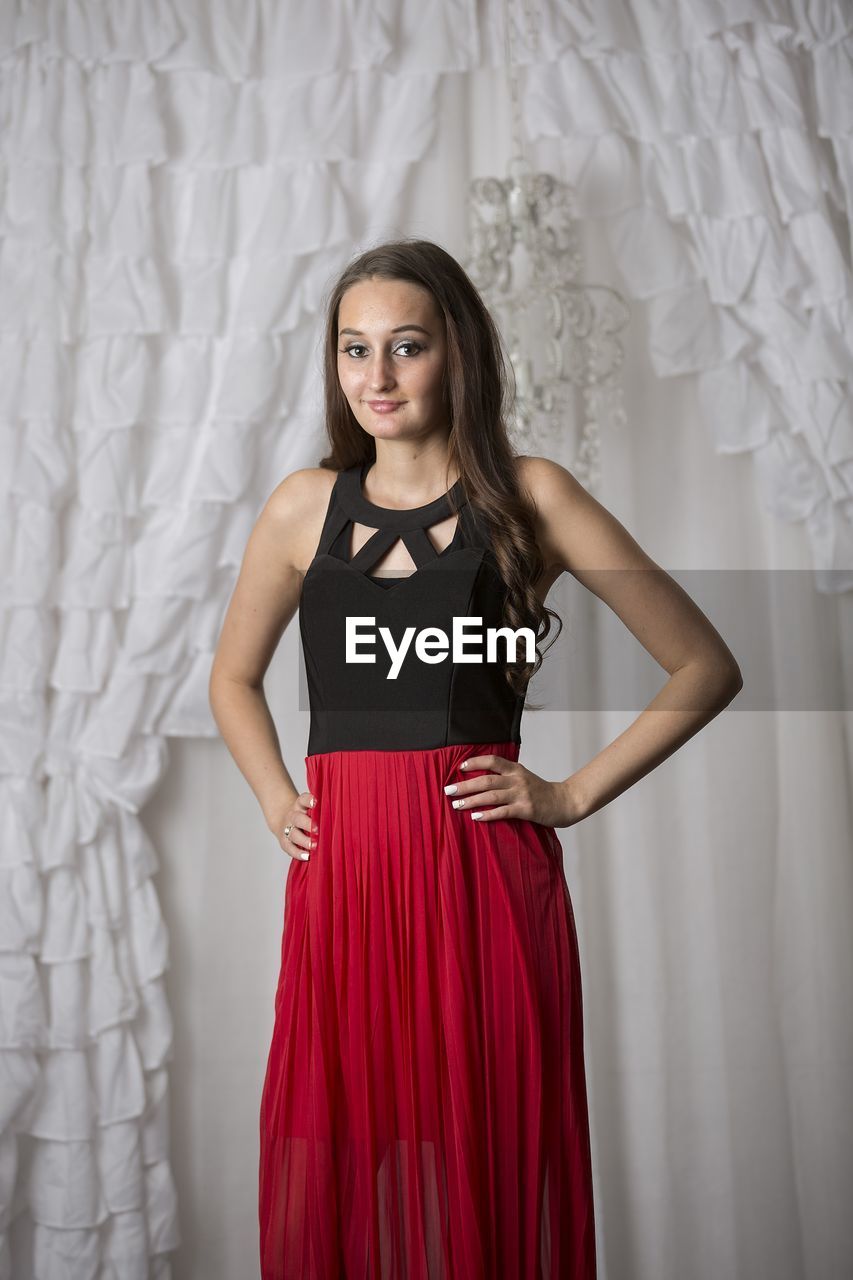 Portrait of young woman standing against curtain