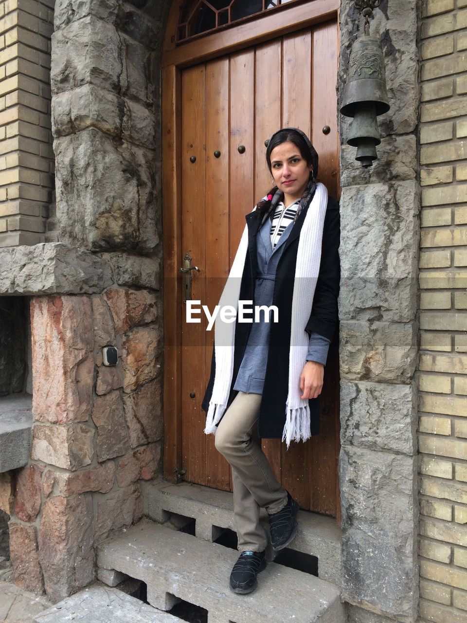 Young woman standing on doorway by antique bell