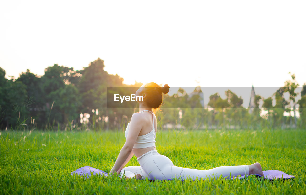 rear view of woman doing yoga on field against sky