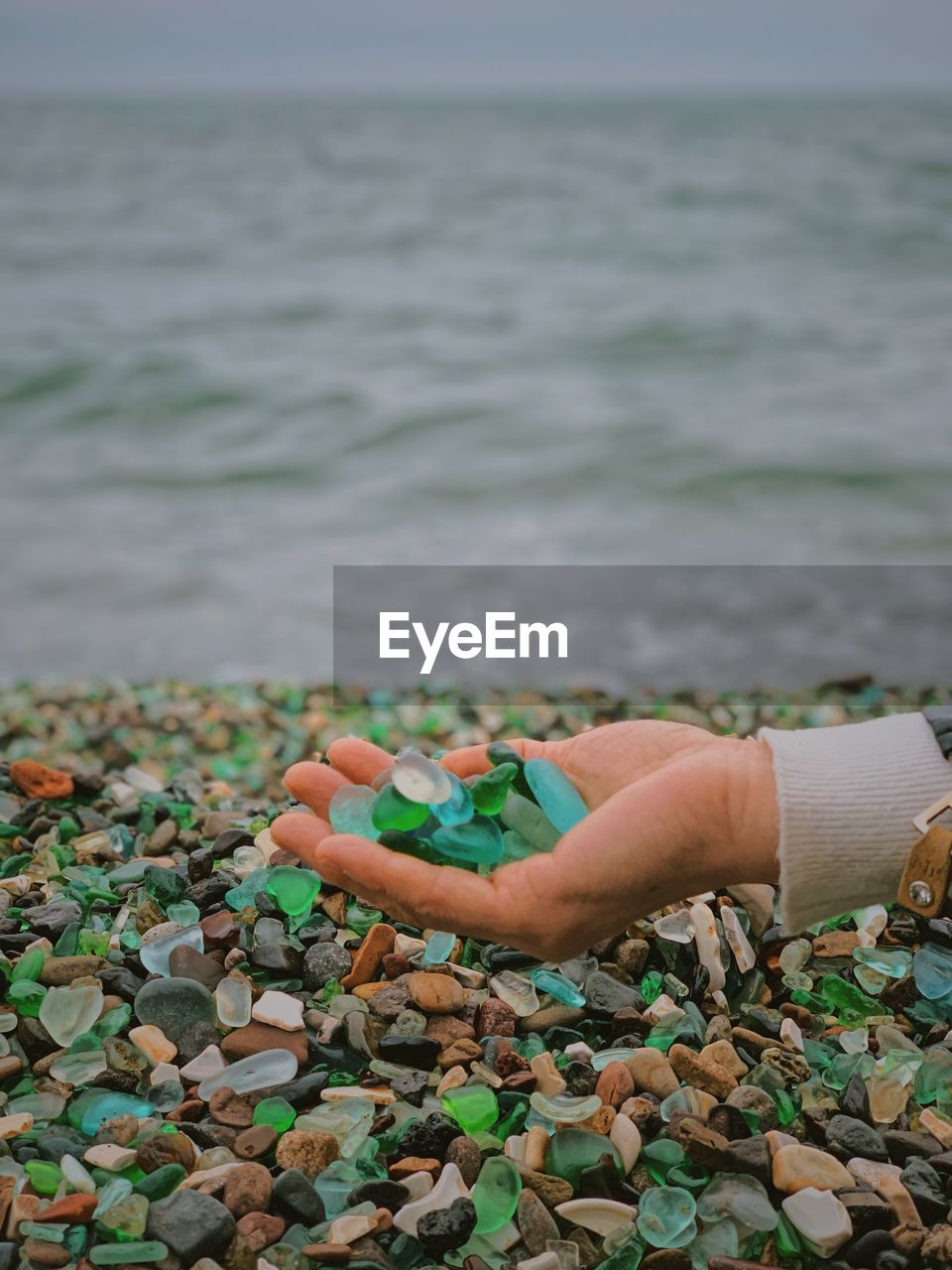 Person holding pebbles against sea