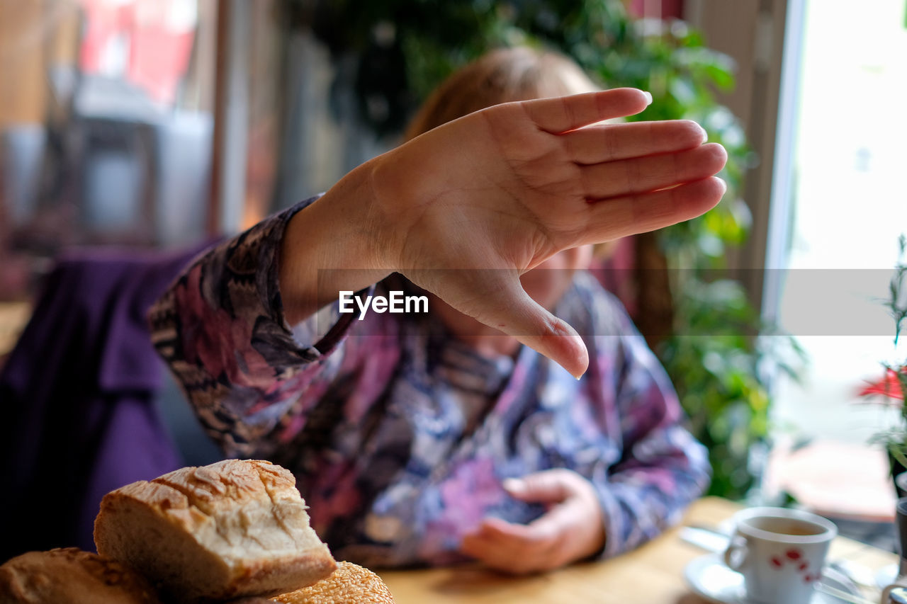 Woman covering her face with hand while sitting by breads on table