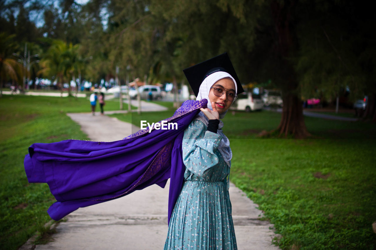 PORTRAIT OF SMILING YOUNG WOMAN STANDING BY TREES