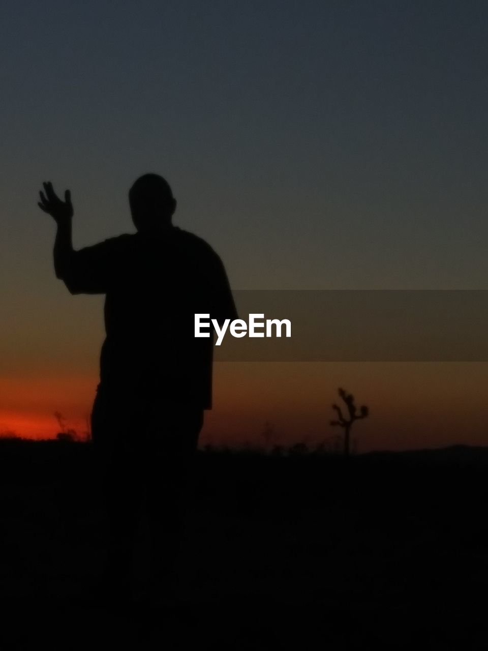 SILHOUETTE MAN STANDING ON FIELD AT SUNSET