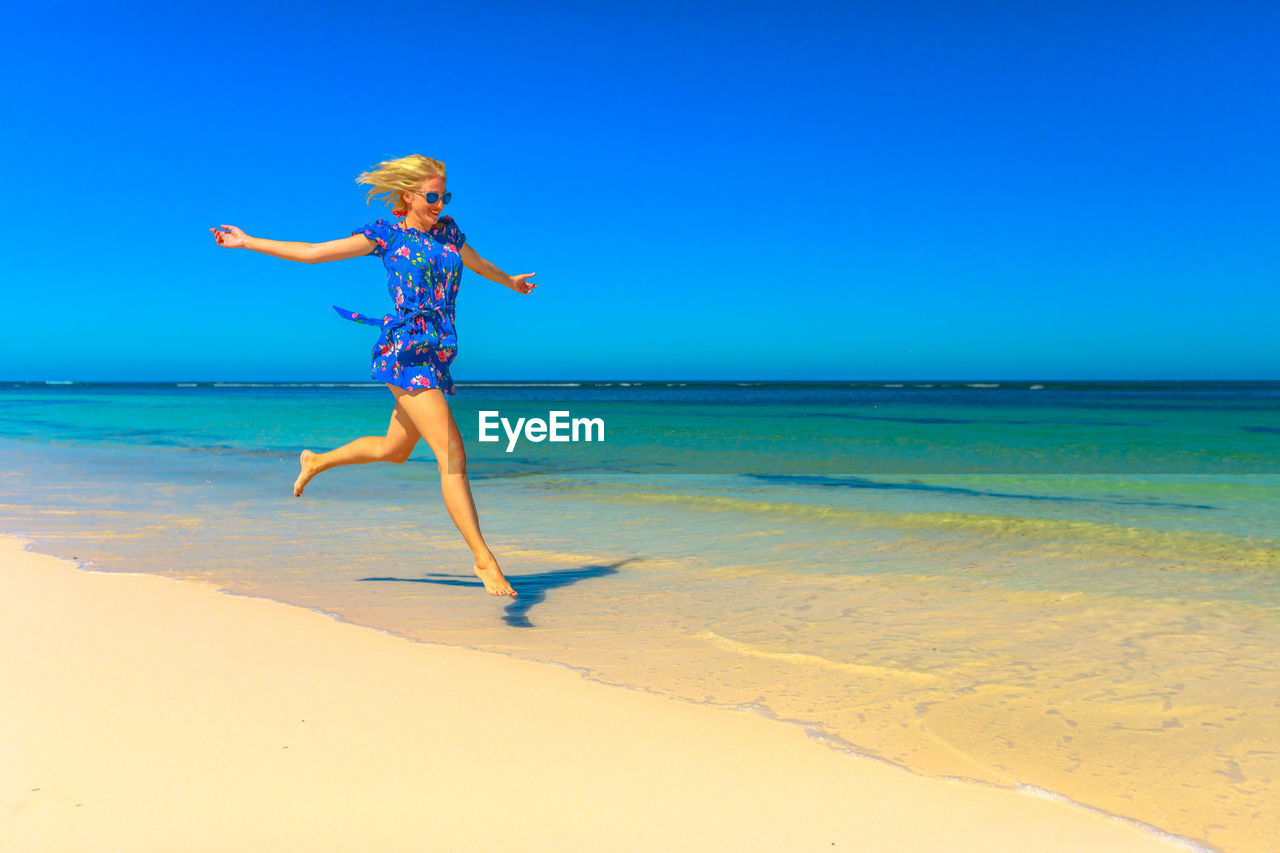 Full length of woman jumping on shore at beach during sunny day