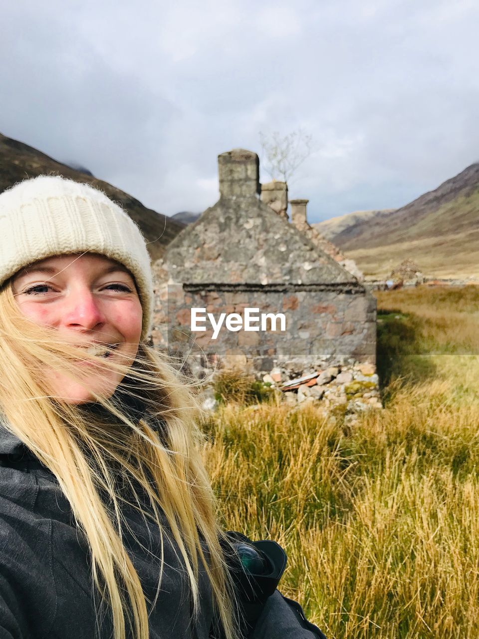 Portrait of woman on grass against old house and sky