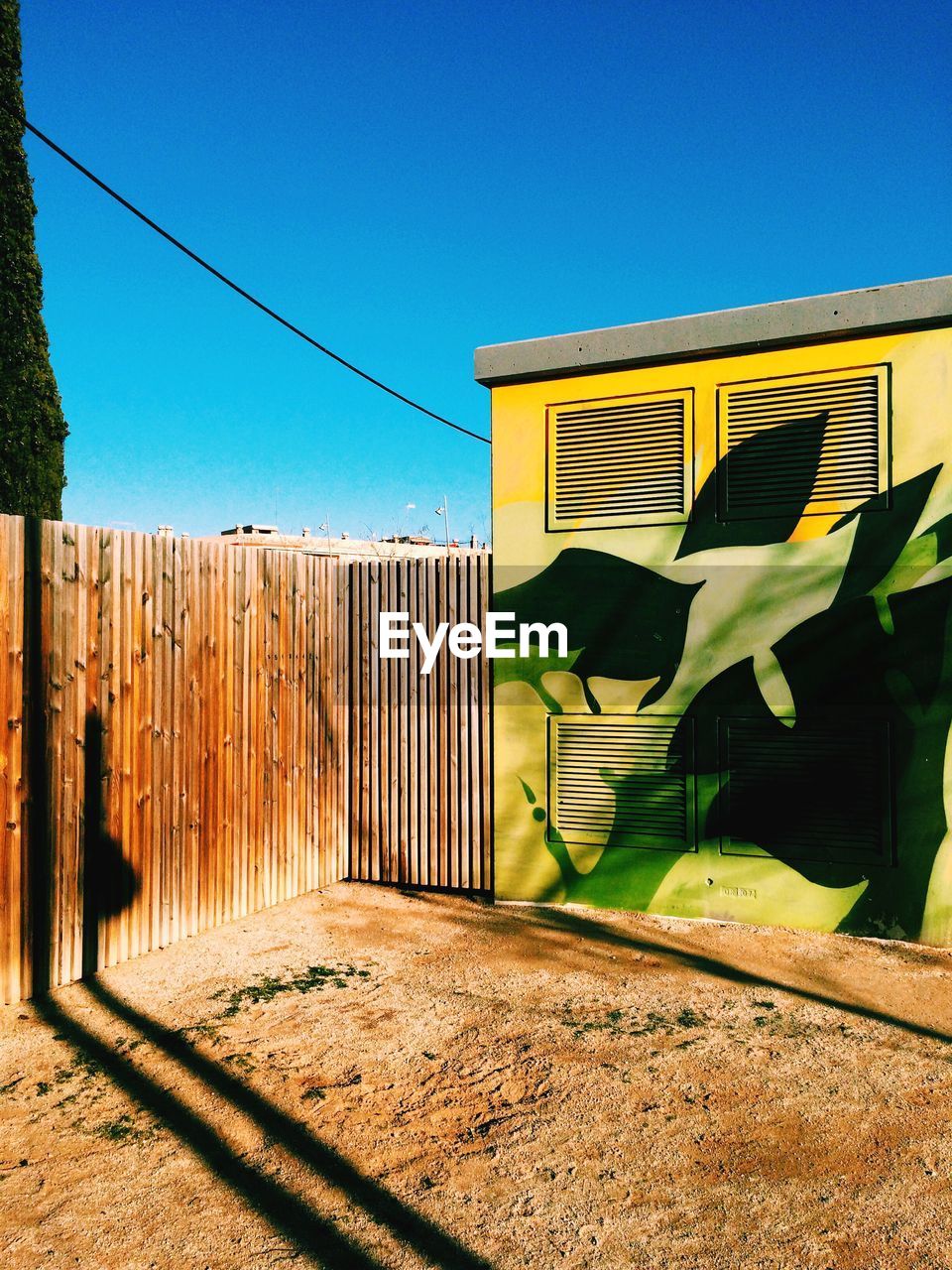 Graffiti on cabin by wooden fence against clear blue sky
