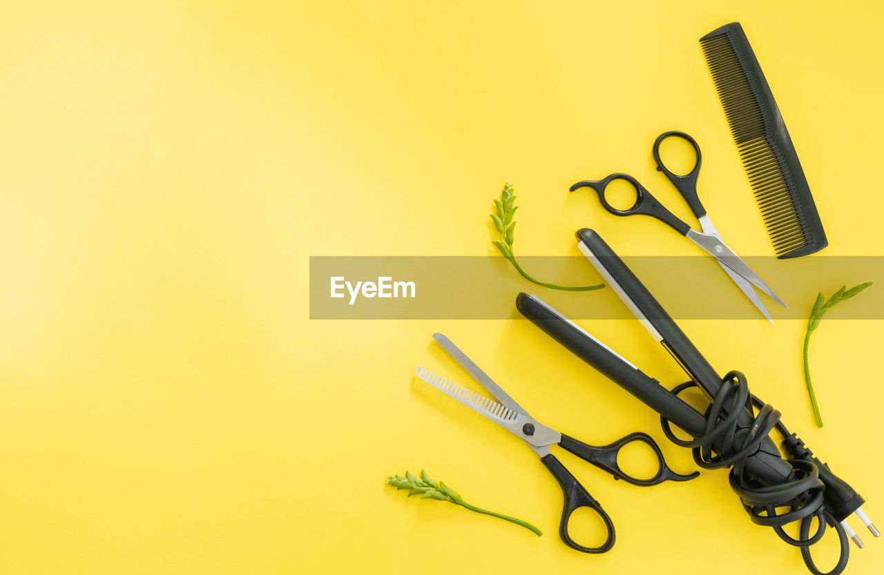 Scissors and other hairdresser's accessories on yellow background, flat lay. space for text