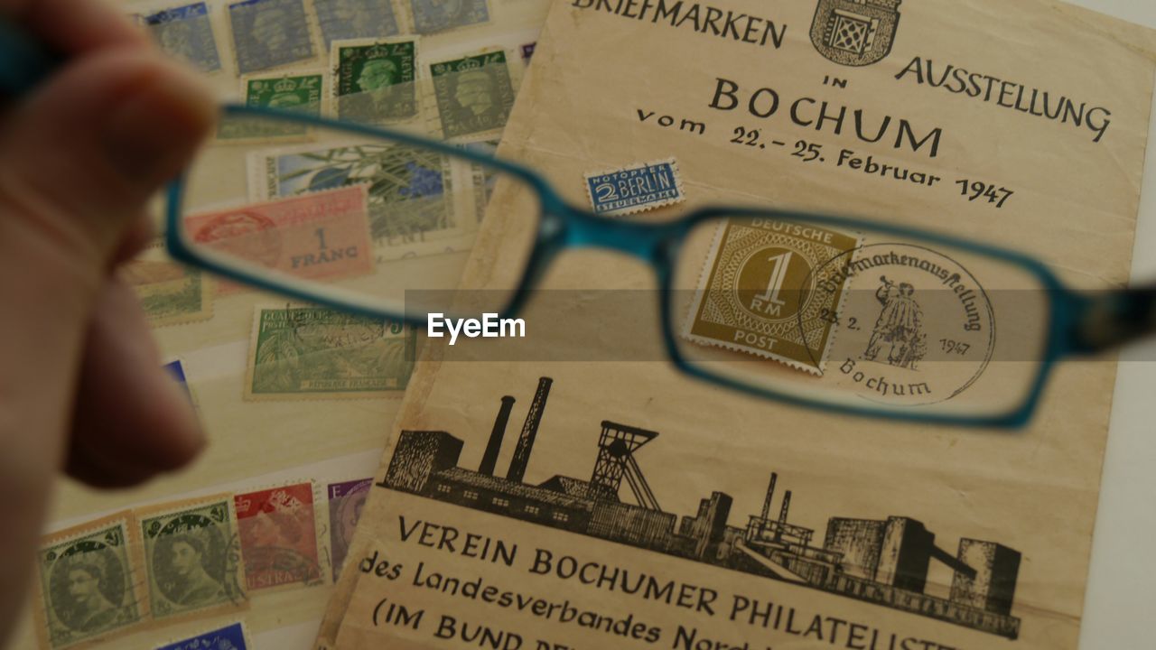 Cropped hand holding eyeglasses over postage stamps