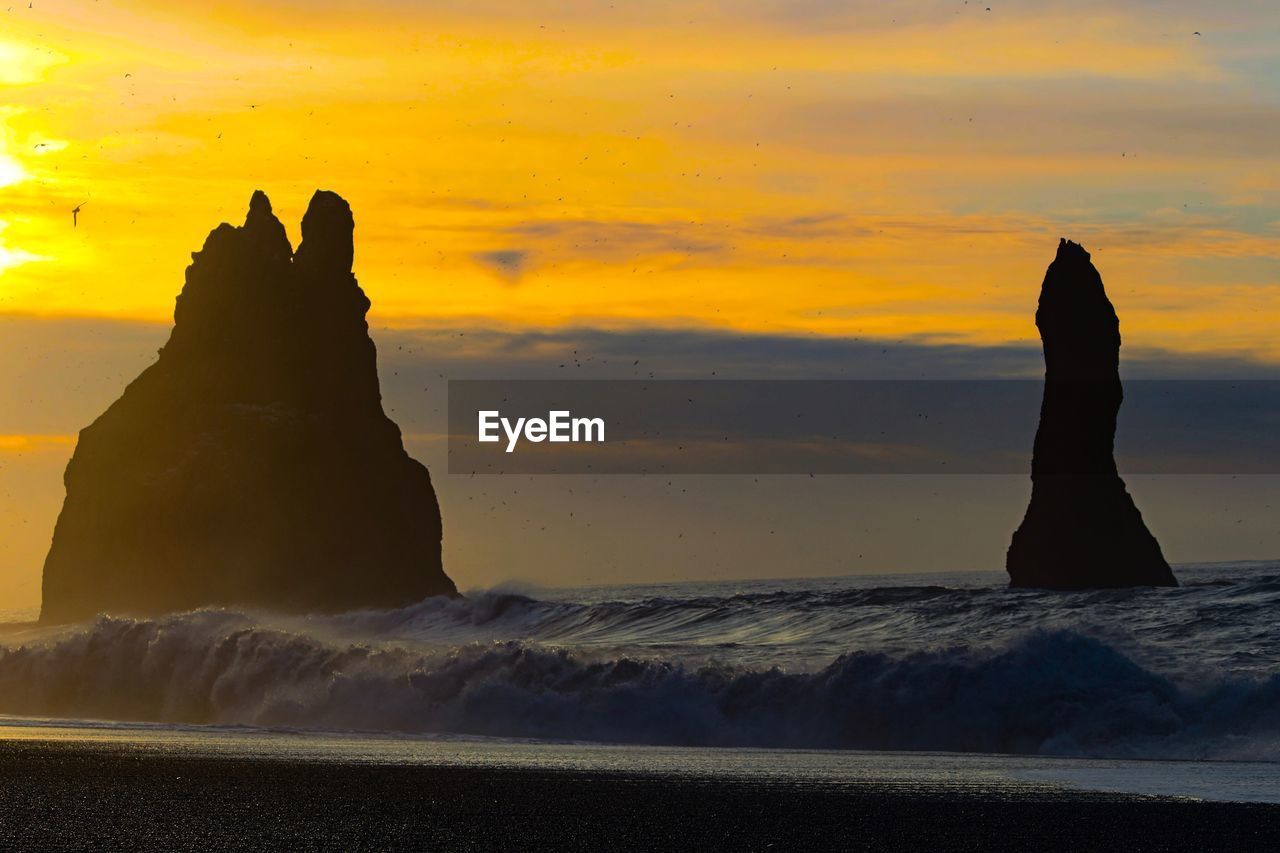 Silhouette rock formation on beach against sky during sunset