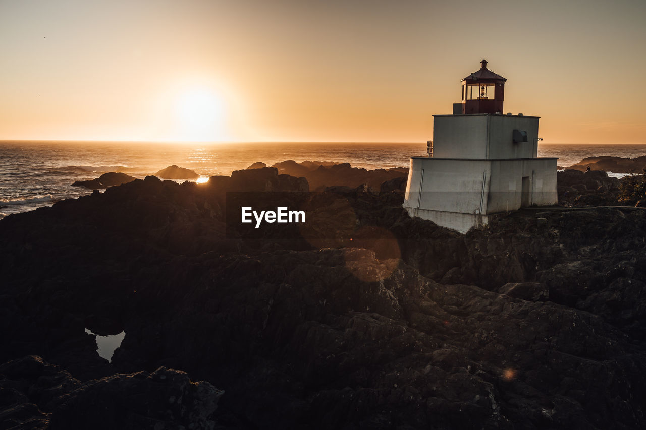 Lighthouse by sea against sky during sunset