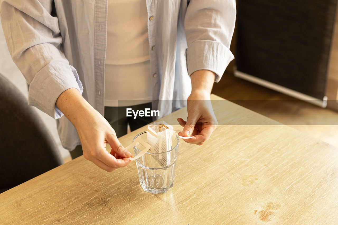 Young woman unpacks a bag of filter coffee and puts it in a glass, hand view