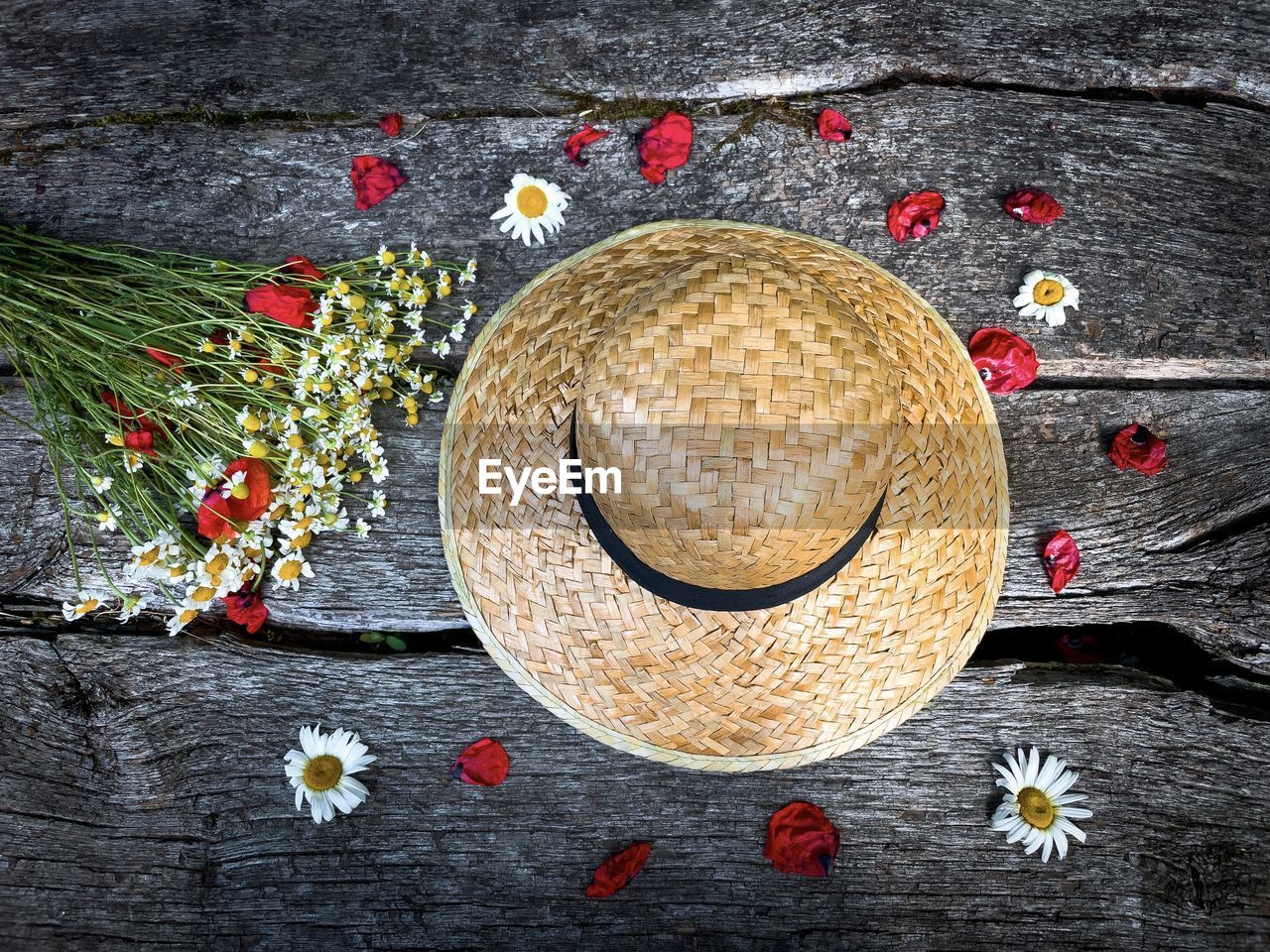 Summer flat lay consisting of straw hat, poppy petals and flower bouquet on rustic wooden table
