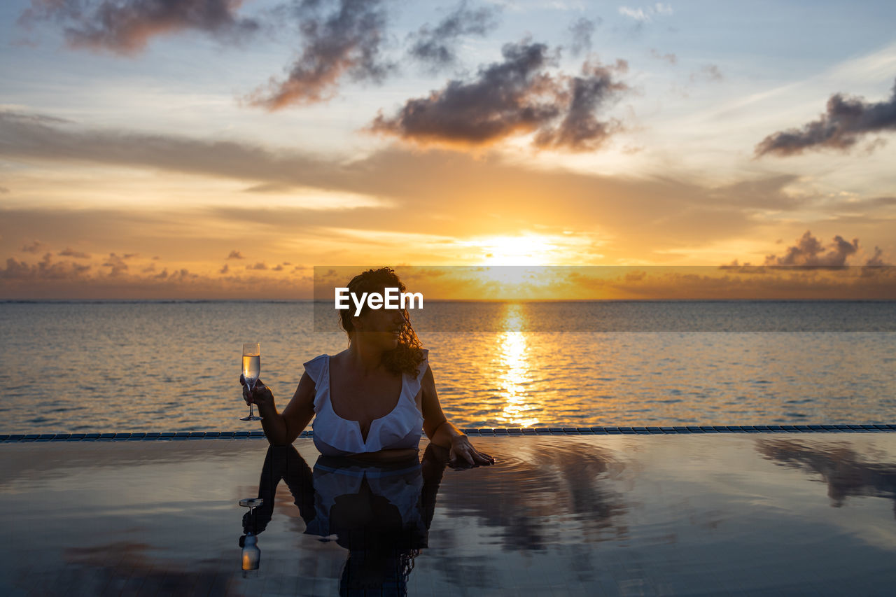 Attractive woman on a infinity pool near the ocean with a glass of champagne