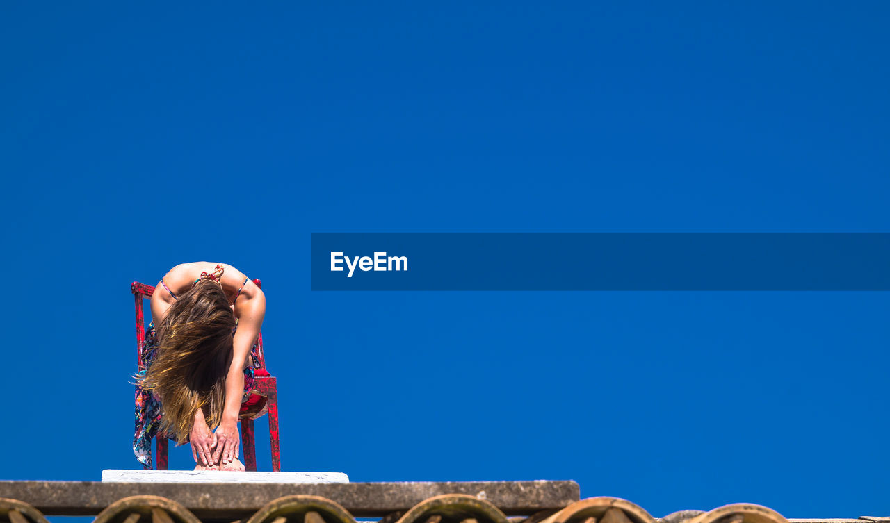Low angle view of woman against clear blue sky