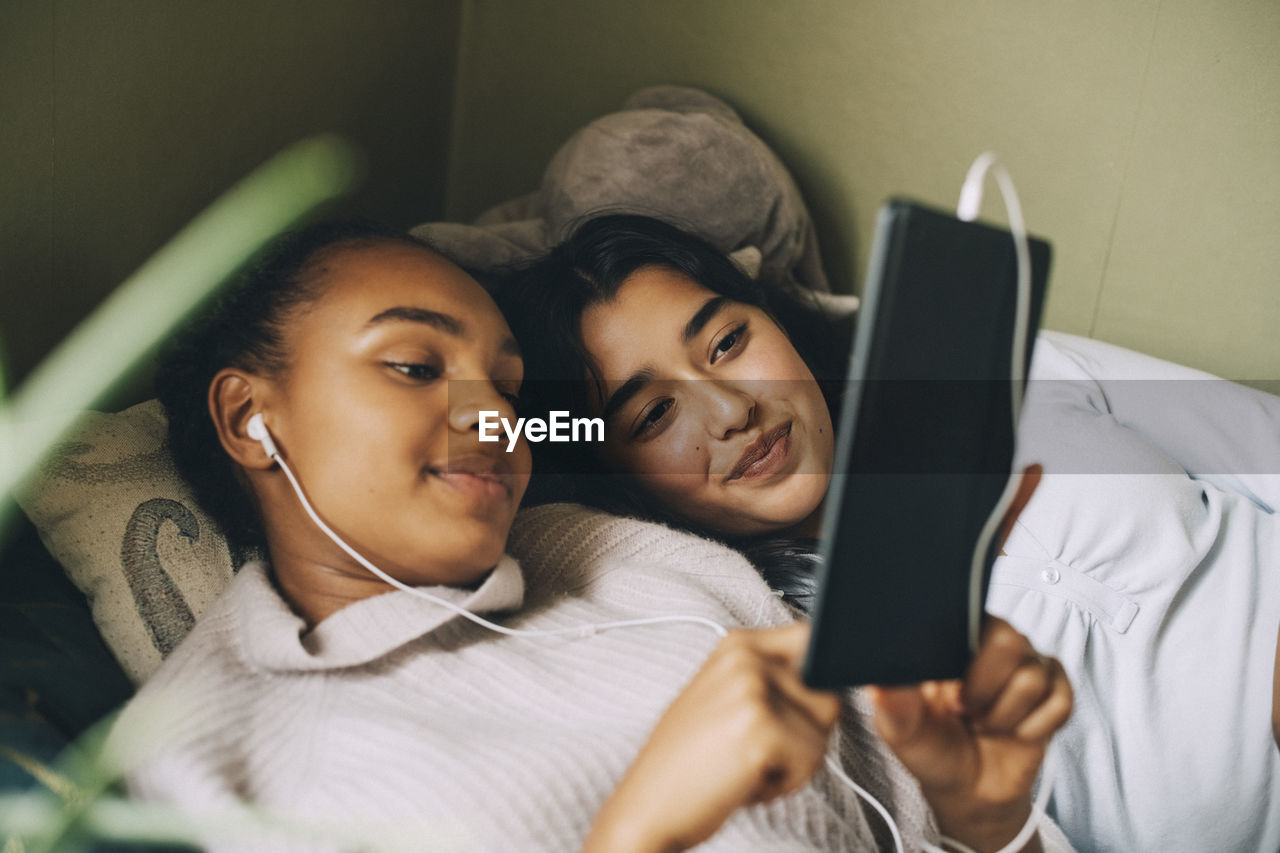 Female teenagers listening music on digital tablet while lying on bed at home