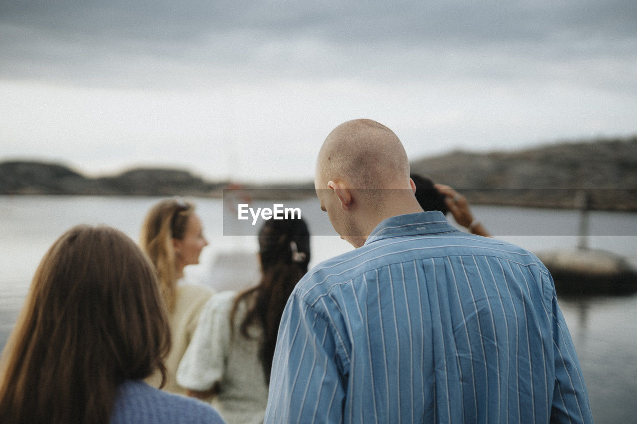 Rear view of man and woman enjoying with friends near lake