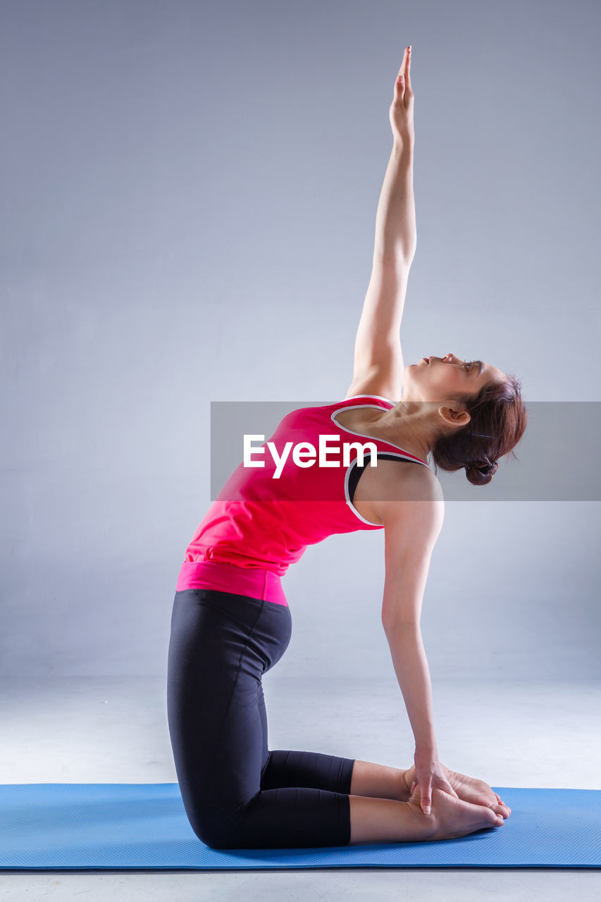 Woman balancing while practicing over exercise mat against gray wall