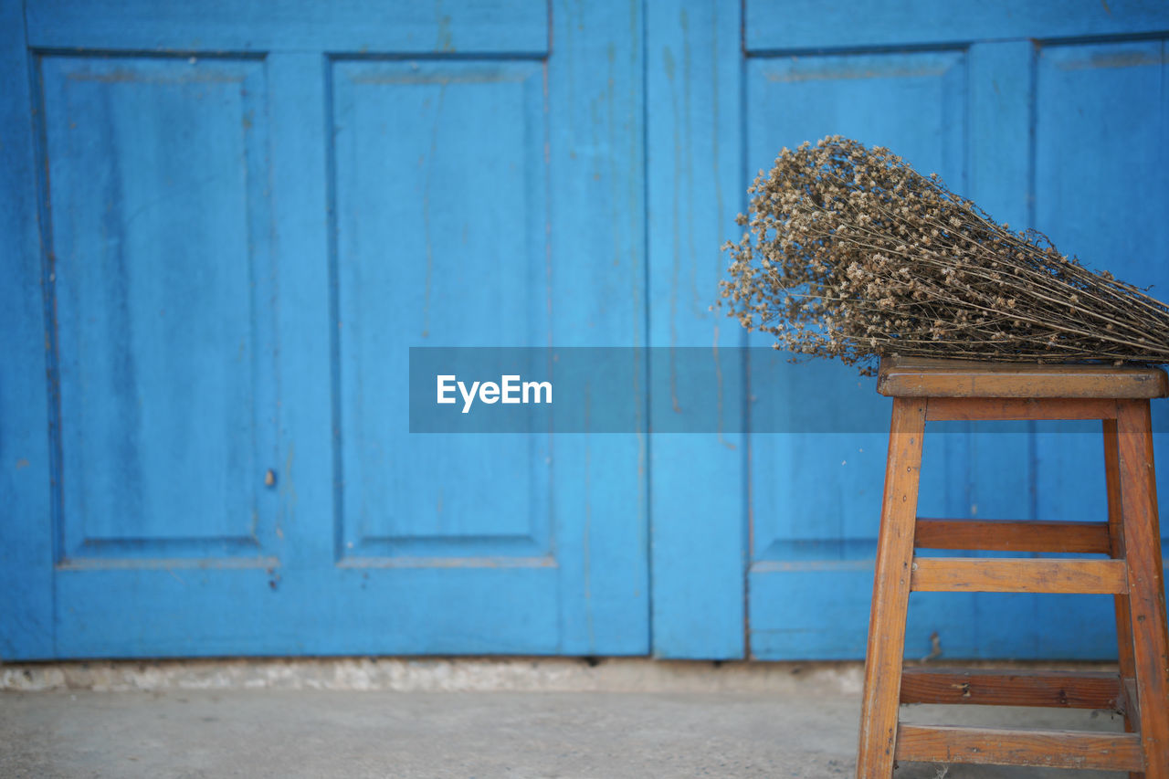 Dried flower bouquet on wooden chair near blue door