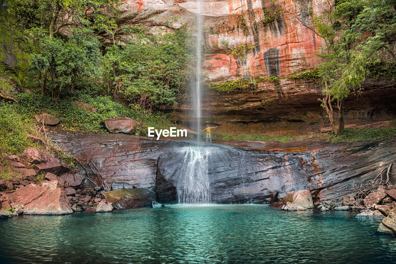 Low angle view of man standing on mountain by waterfall