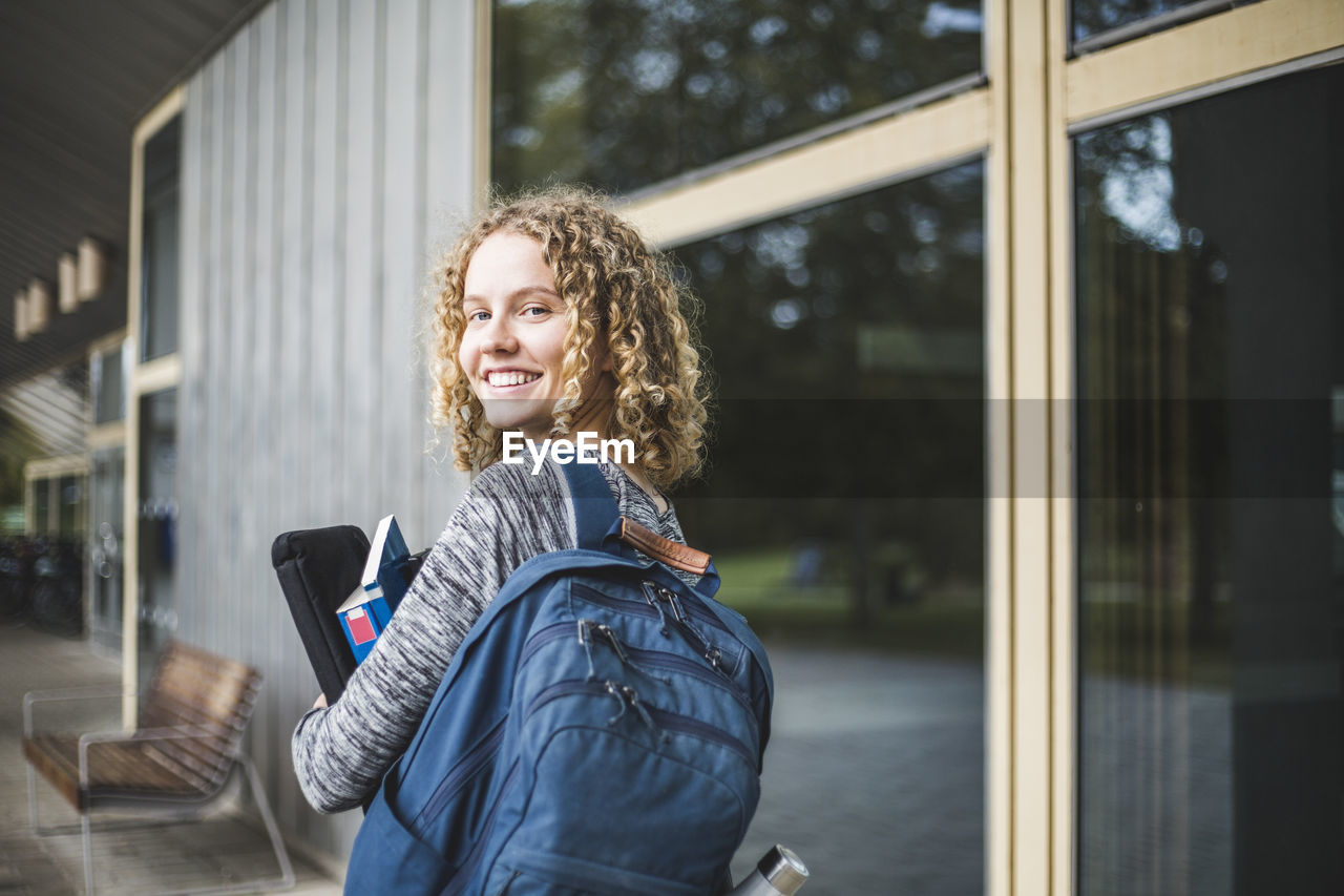 Portrait of smiling young woman with bag at university campus