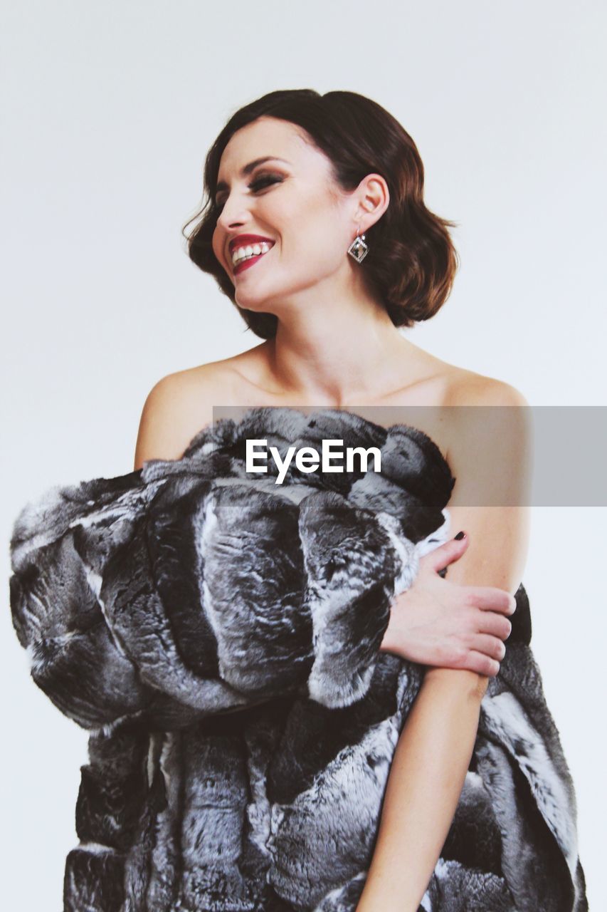 Smiling young woman holding jacket against white background