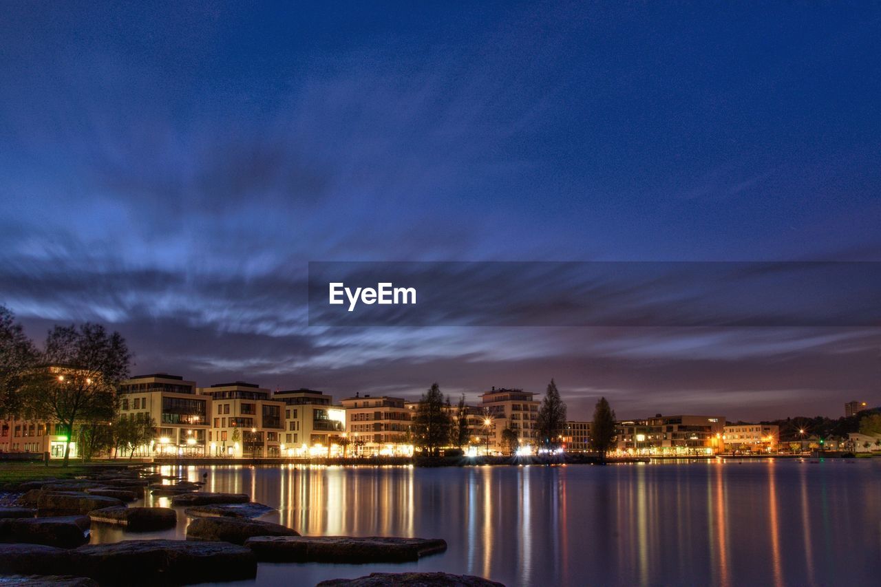 River by illuminated city against sky at dusk