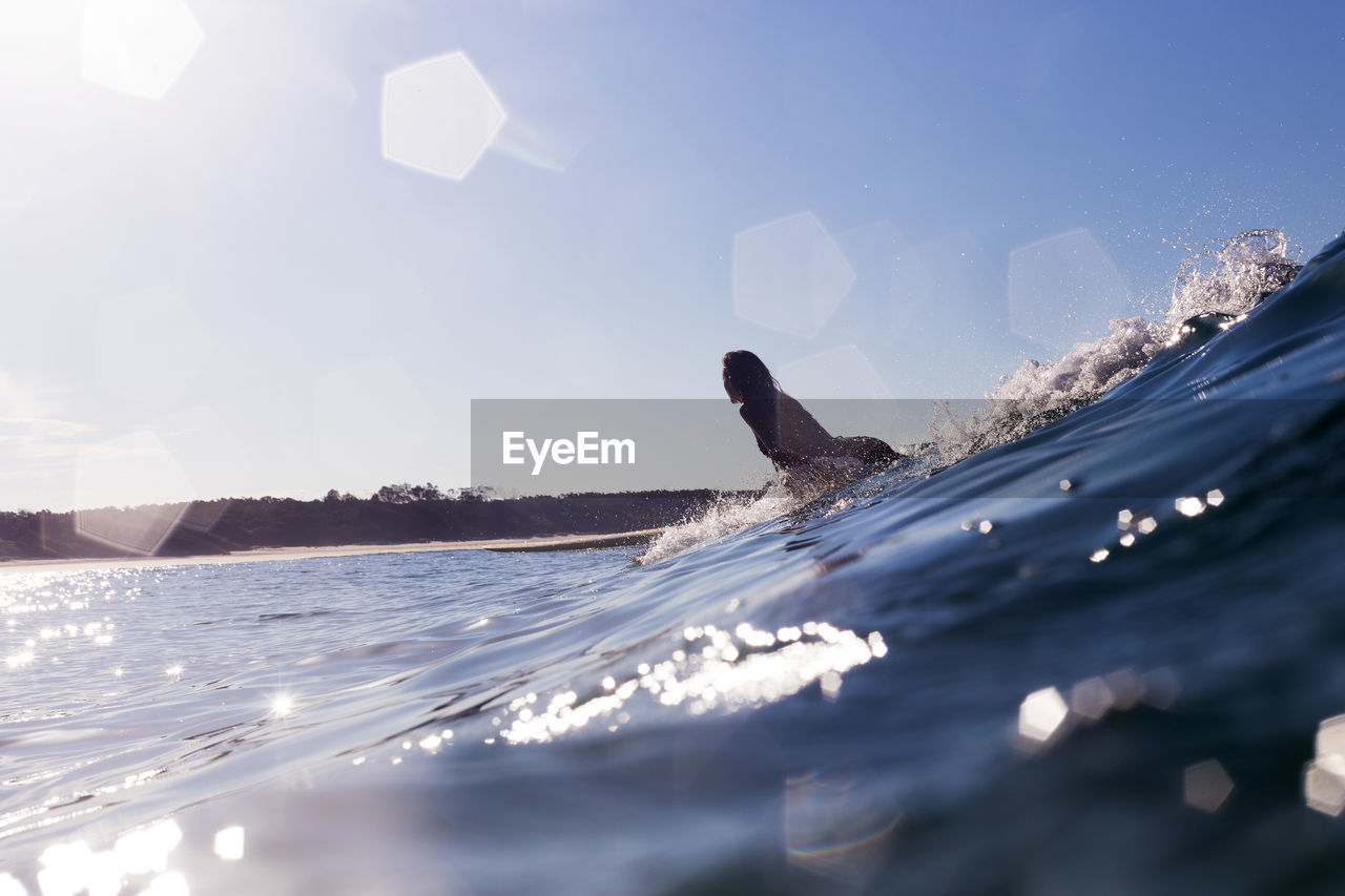 Woman surfing in sea against blue sky