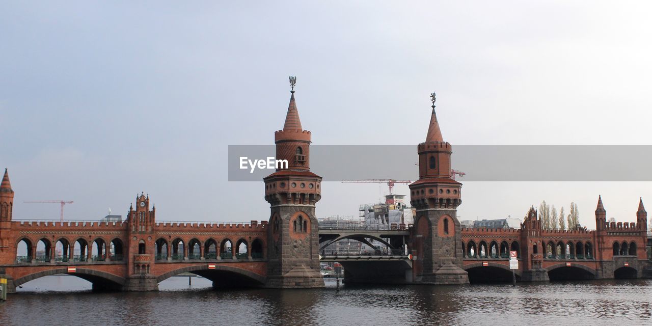 Bridge over river by buildings against sky in city