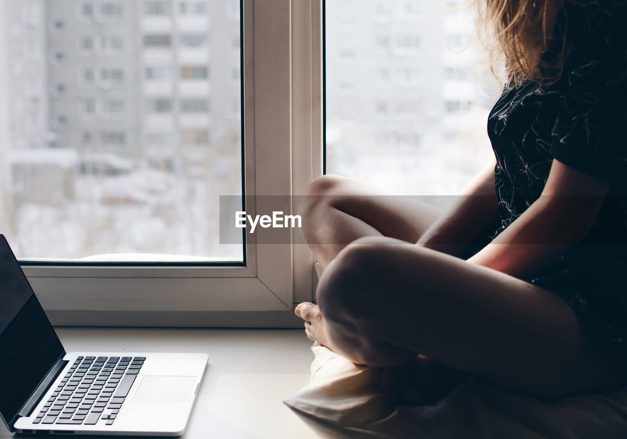 Low section of woman sitting by laptop at home